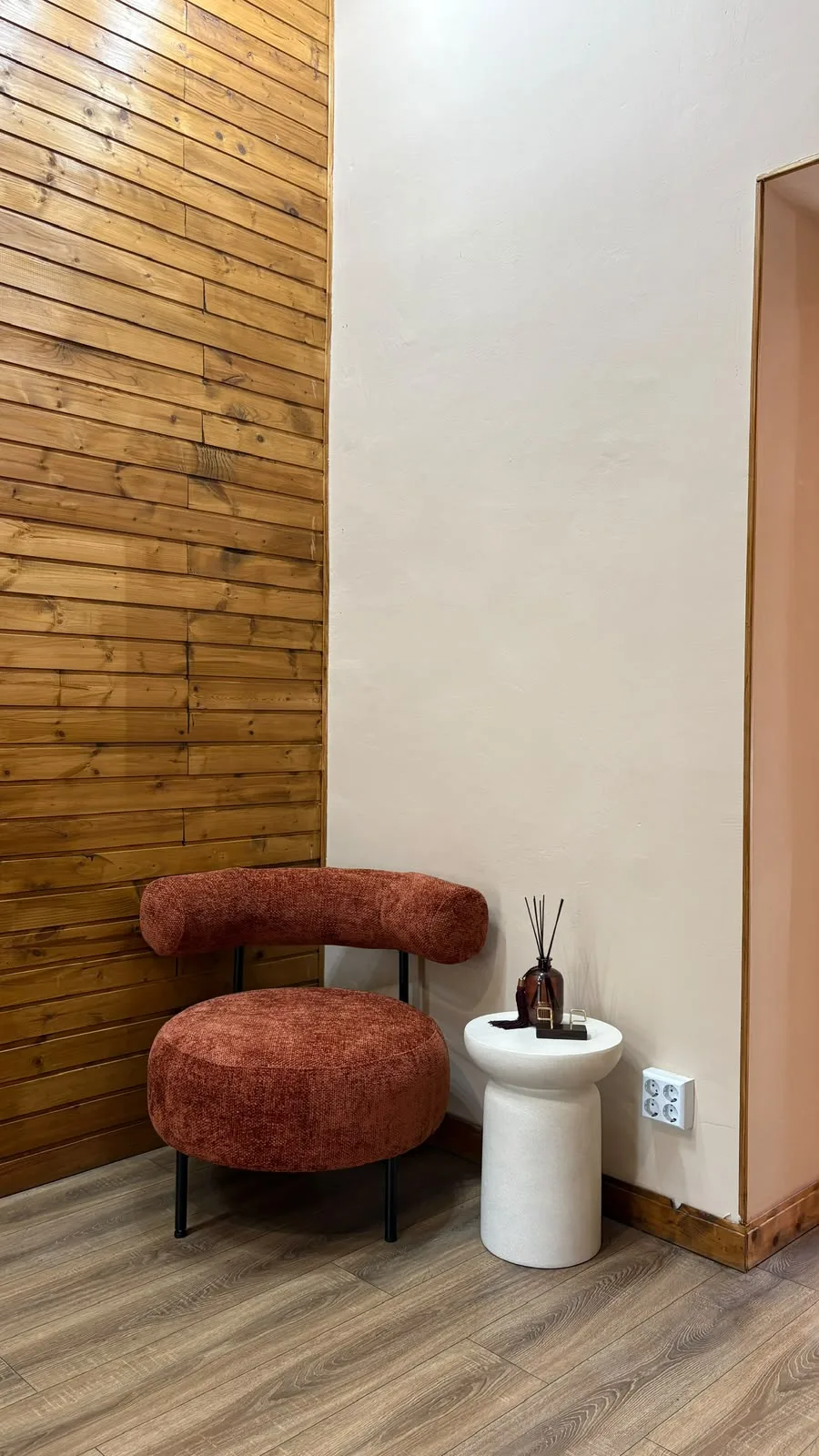 Colț din studio cu fotoliu rotund terracotta, măsuță albă și difuzor de parfum